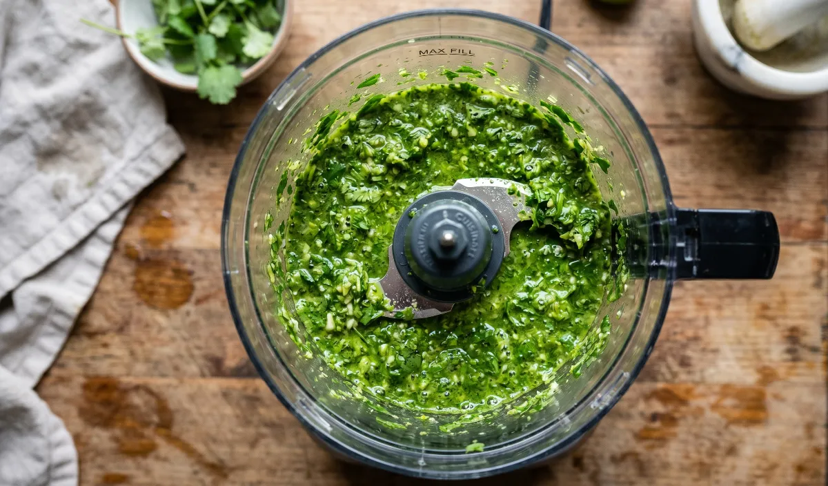 food processor bowl filled with the vibrant, bright green cilantro-lime marinade.