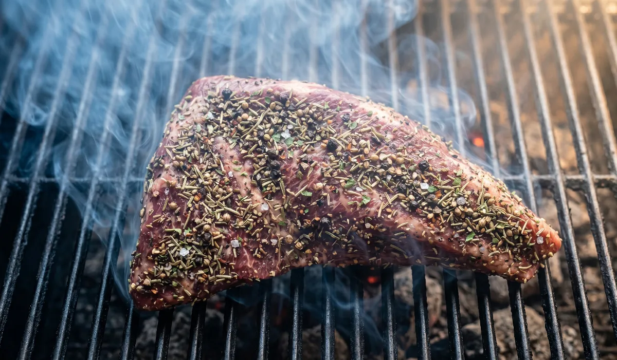 The tri-tip resting on the smoker grates, bathed in a light, translucent blue smoke